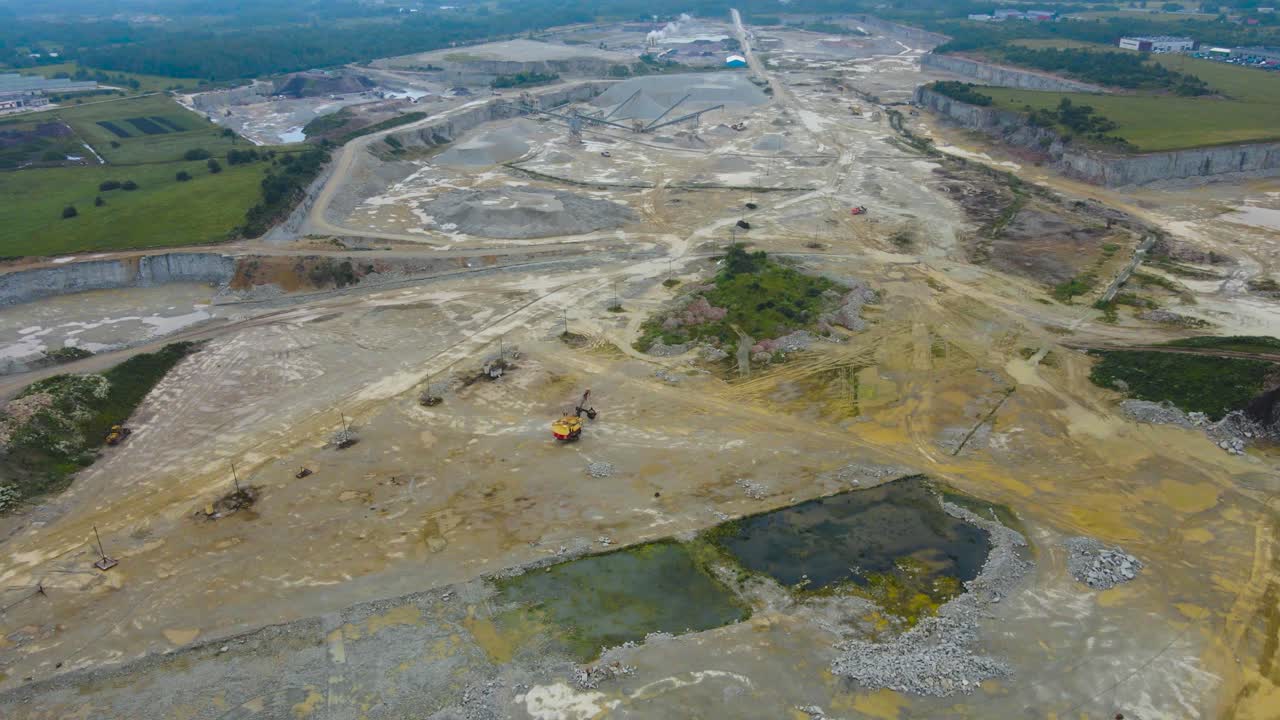 Aerial drone footage flying backwards and revealing a large limestone quarry mine during a wet and damp summer day after rain, with mining equipment machines and conveyor belts visible in the back