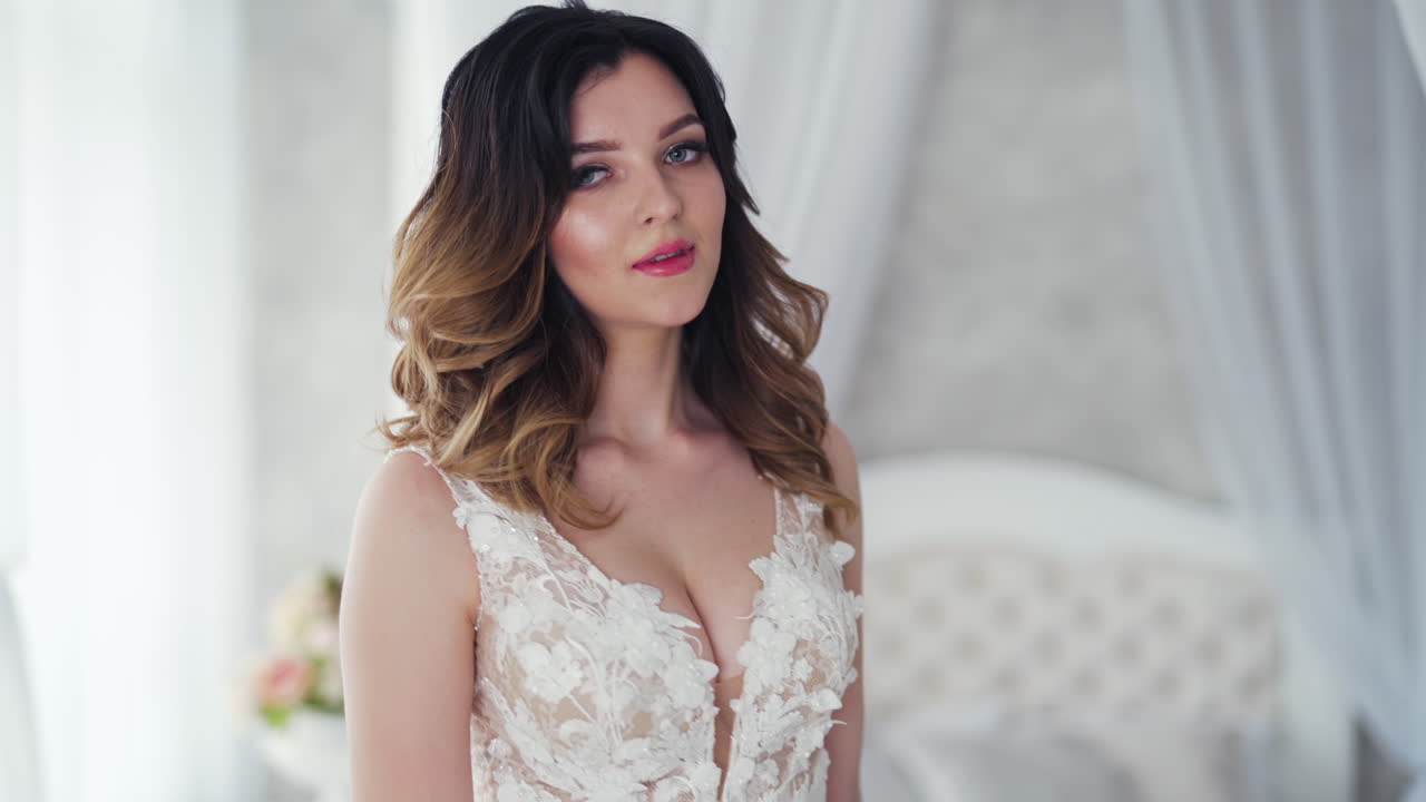 Gorgeous young model in a long white dress is posing in front of camera. Luxurious bride in a wedding dress holding flowers is spinning in a light studio.