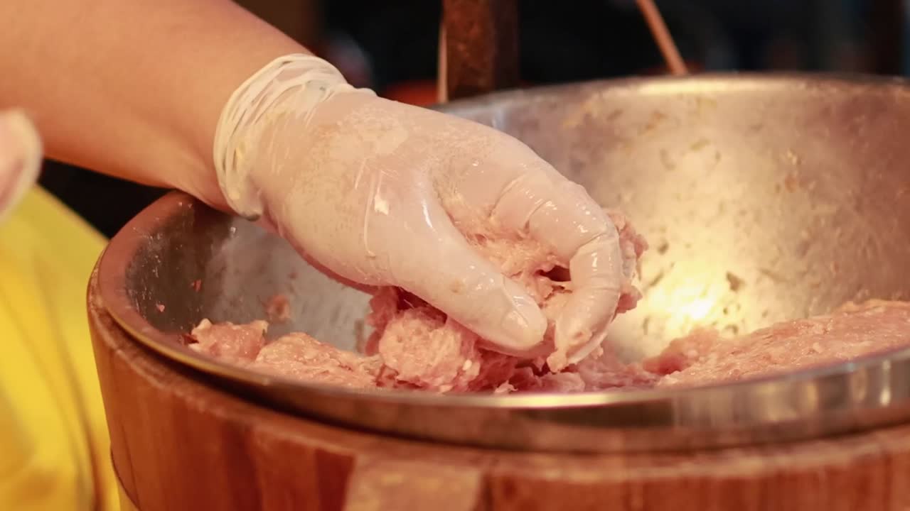 Close-up of gloved hands skillfully mixing minced meat in a wooden bowl, showcasing detailed food preparation.