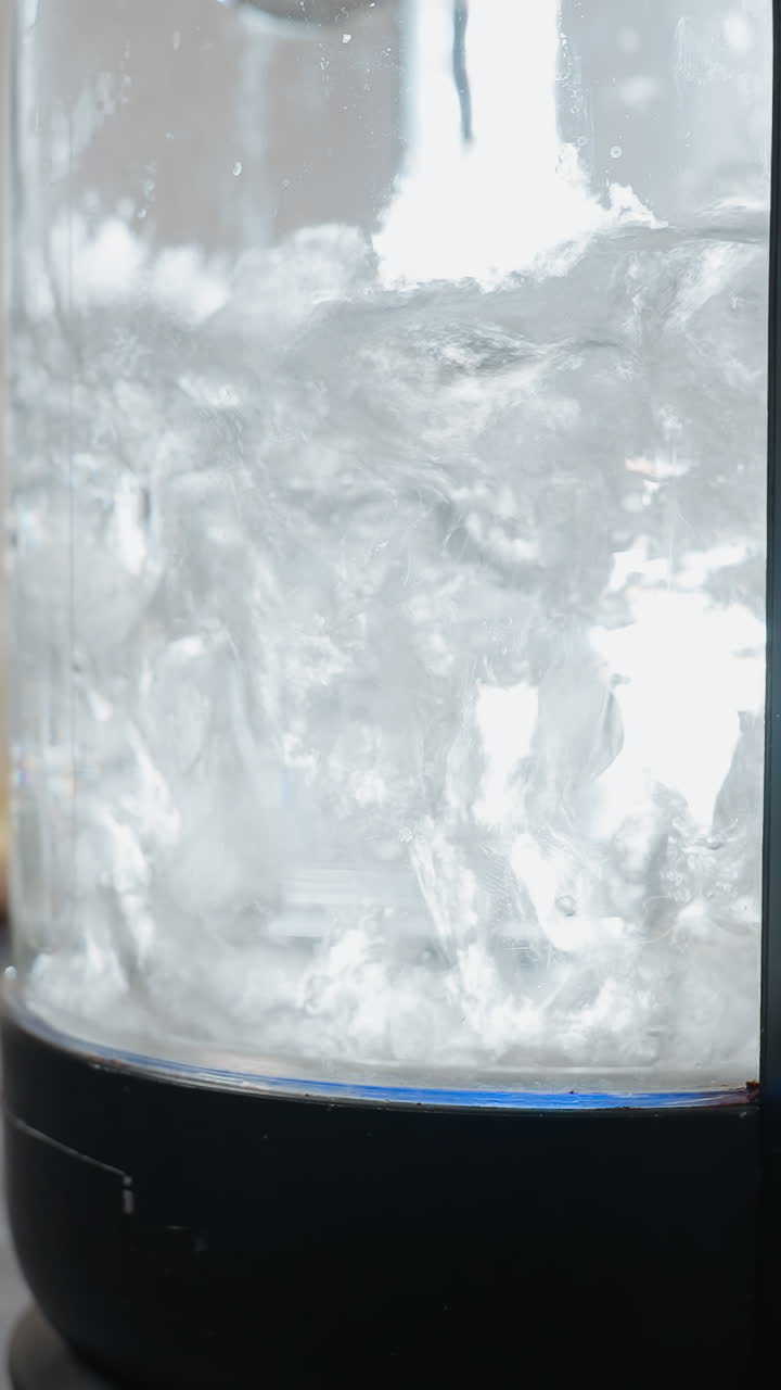 은 푸른 빛과 함께 거품이 형성되고 상승하는 투명한 항아리에서 빠르게 는 물의 근접, 배경에는 다양한 부 장비와 흐릿한 물체가 있습니다.