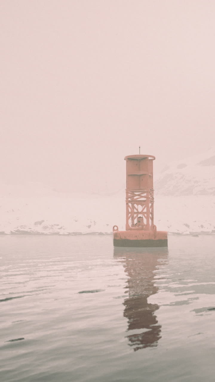 Winter fog covers a lighthouse in a serene harbor during quiet morning hours