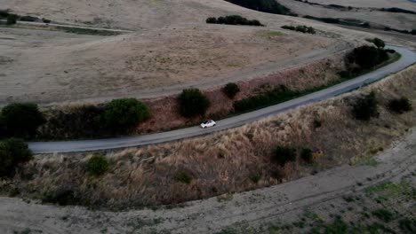 A-drone-follow-with-a-pan-left-movement-a-Fiat-500-through-the-country-hills-street-of-Ascoli-Satriano-in-Puglia