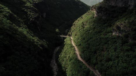 aerial view of a green mountain with small road and a bridge. orbit ascending.