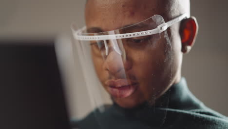 African-American-man-with-face-shield-works-on-tablet