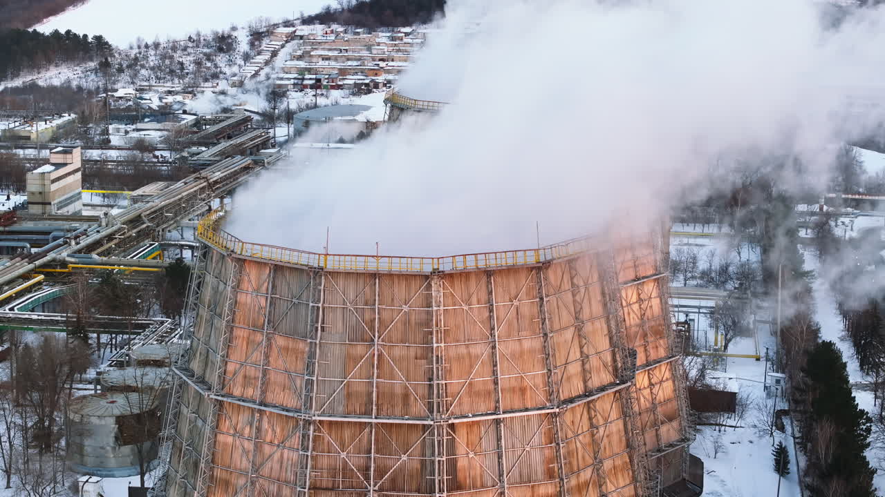 Aerial drone view of a working thermal power station in Chisinau at sunset. City covered in snow. Steam and smoke coming from pipes. Moldova