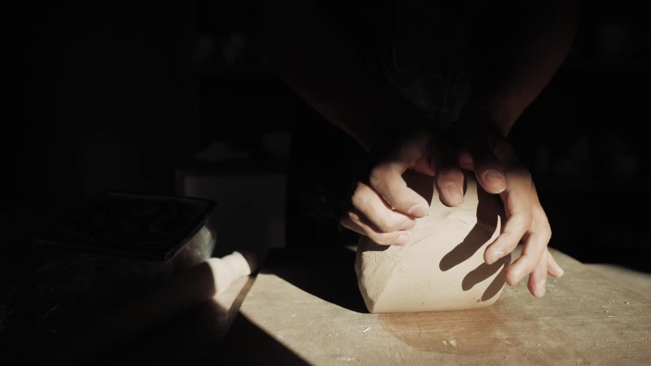 Men's hands are kneading clay on the table in a ray of sunlight. Close-up