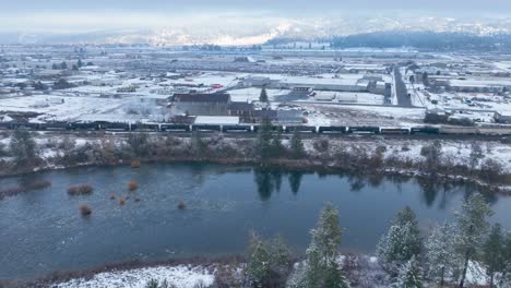 aerial view pushing over a river and towards a train with snow covering the surrounding ground