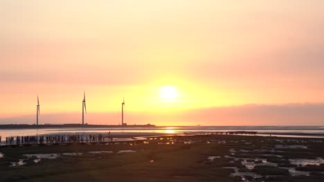 Tourists-walking-on-the-walkway-platform-at-Gaomei-wetland-preservation-area-at-golden-hours,-a-famous-sunset-spot-in-Taichung-city,-Taiwan,-Asia