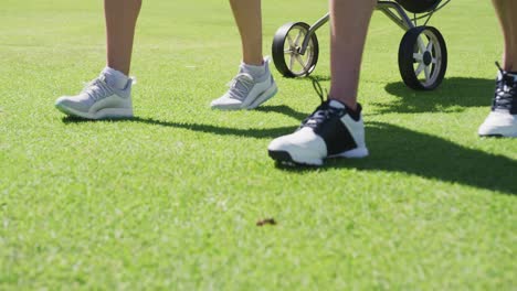 Two-caucasian-women-playing-golf-carrying-bag-filled-with-golf-clubs