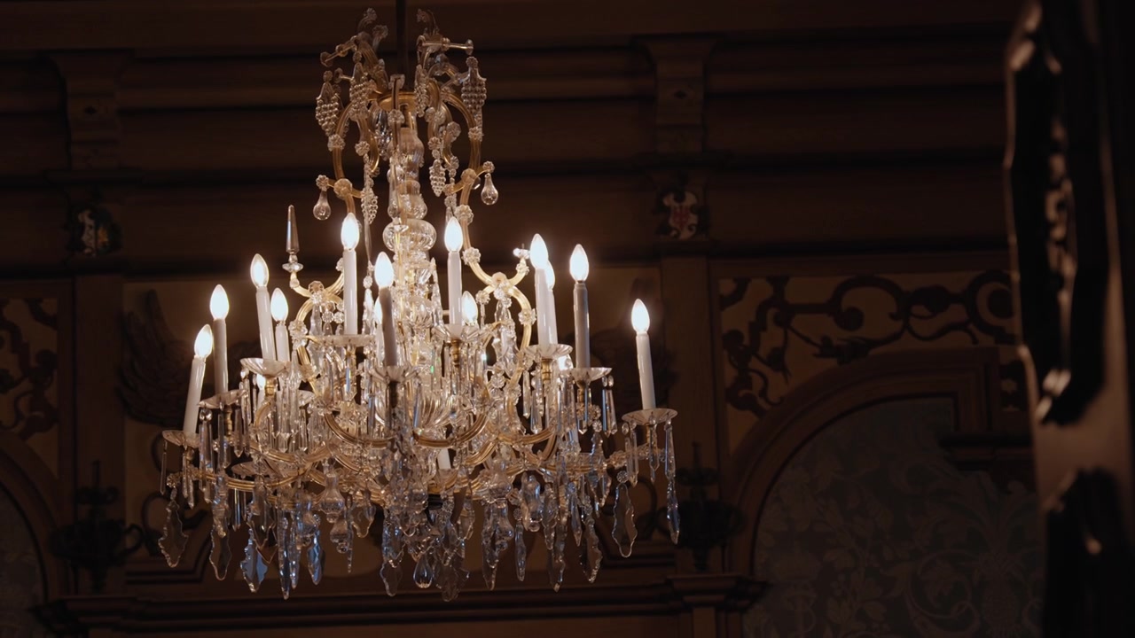 Verzierter Kristallleuchter mit kerzenförmigen Lichtern, leuchtend in einem dunklen historischen Interieur, der klassisches Design, Glasdetails und luxuriöses Dekor hervorhebt.