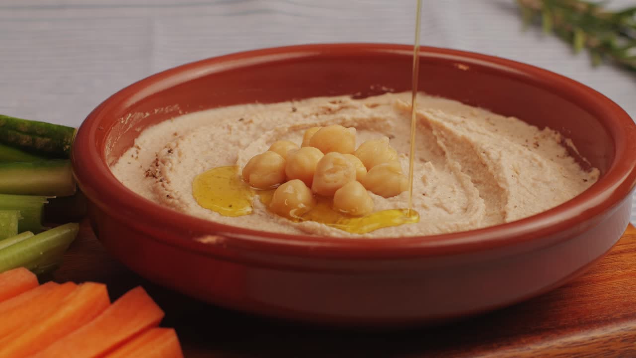 Hummus among fresh vegetables on table close-up. Pouring vegetables slice in hummus. Hummus or fava, a healthy snack of legumes and chickpeas. Kosher healthy vegan food. Lean, vegetarian dish. High quality 4k footage