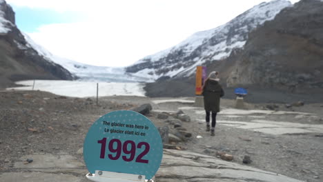 mujer caminando por la marca del año 1992 del glaciar athabasca, retirándose del campo de hielo en alberta, canadá