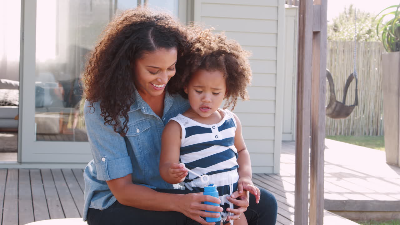 Mixed race mother and daughter blowing bubbles in garden