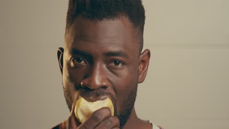 retrato de un joven afroamericano barbudo mordiendo una manzana amarilla