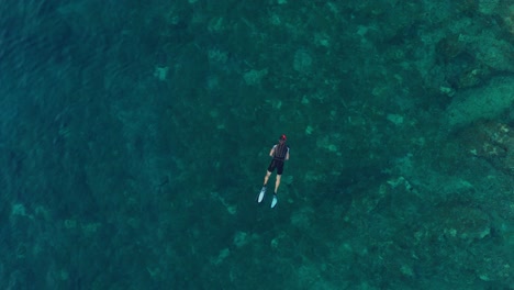 Aerial-view-of-man-snorkeling-in-crystal-clear-turquoise-water,-rocky-beach