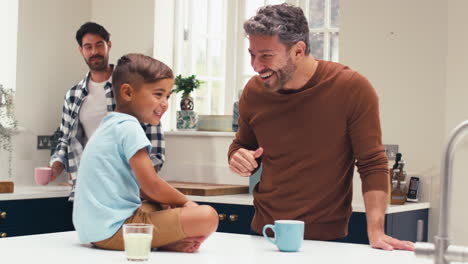 Same-Sex-Family-With-Two-Dads-In-Kitchen-With-Son-Sitting-On-Counter-Giving-Parent-High-Five