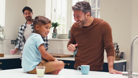 same sex family with two dads in kitchen with son sitting on counter giving parent high five