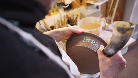 close up of male potter putting lettering onto bread bowl in ceramics studio