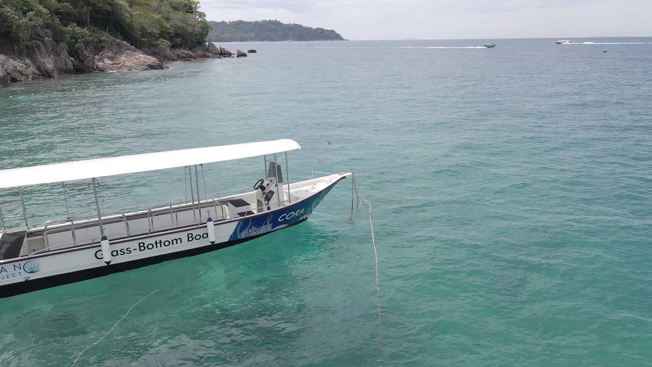 Aerial view of a boat rocking on ocean waves at anchor. Other boats are in the distance traveling between islands. Trucking shot to the right. Filmed in Perhentian Kecil, Malaysia.