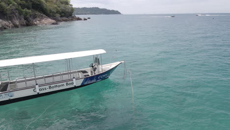 aerial view of a boat rocking on ocean waves at anchor. other boats are in the distance traveling between islands. trucking shot to the right. filmed in perhentian kecil, malaysia.