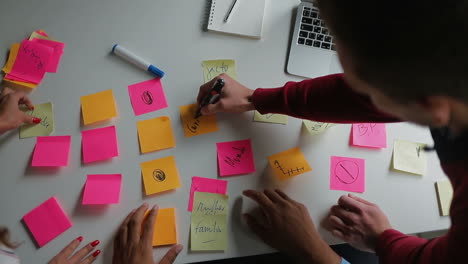 Young-people-glueing-sticky-notes-on-table.