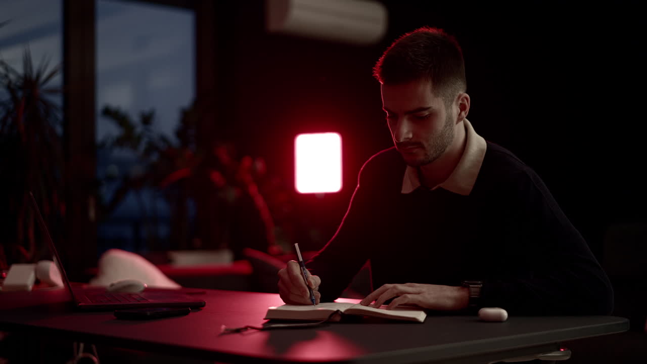 A young man writing in a notebook at a cozy home desk, journaling in warm evening light. Calm atmosphere, self-reflection, focus, and quiet lifestyle moments in a comfortable living room