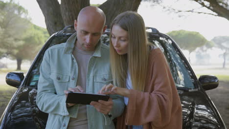 Couple-using-digital-tablet-near-car