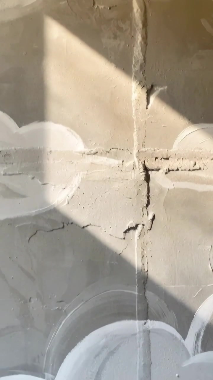 Video verticale: Telecamera che si sposta rivelando nuvole dipinte su una parete intonacata, mostrando una giuntura e un raggio di sole.