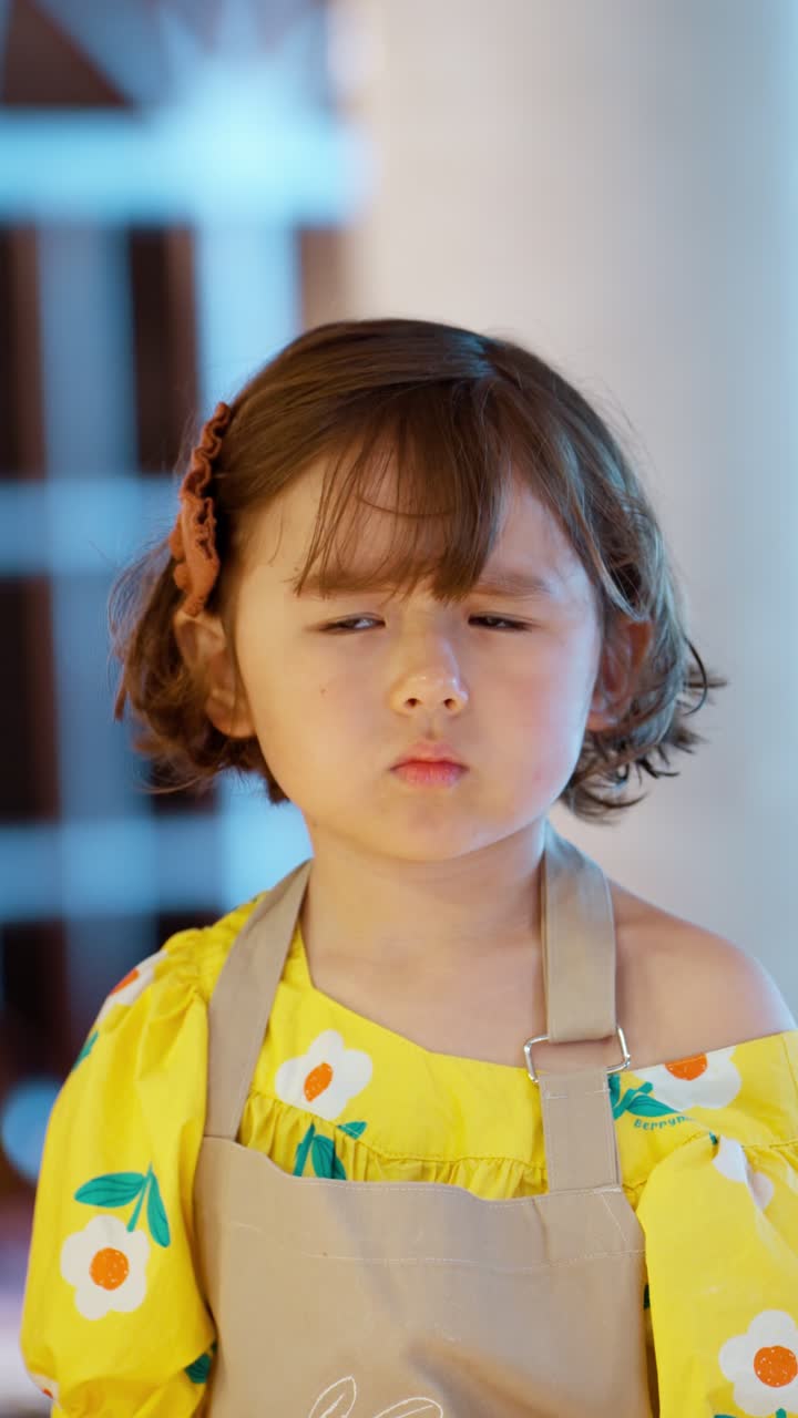 Vertical close-up portrait of a cute little girl in an apron listening attentively to her teacher during a fun cooking class