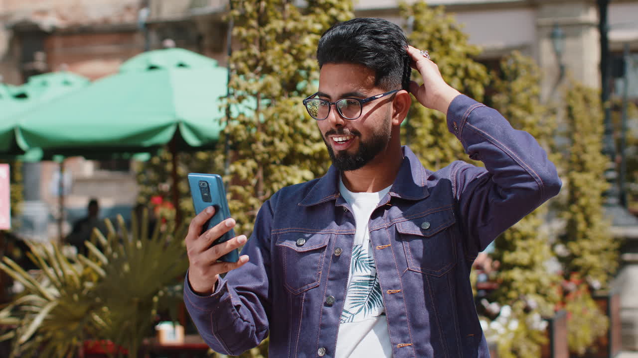 Excited happy winner indian man use smartphone celebrating win good message news in city street