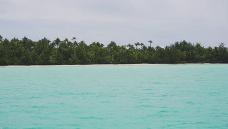 aerial view of clear water with aitutaki island and palm trees during cloudy day, cook islands. wide shot.