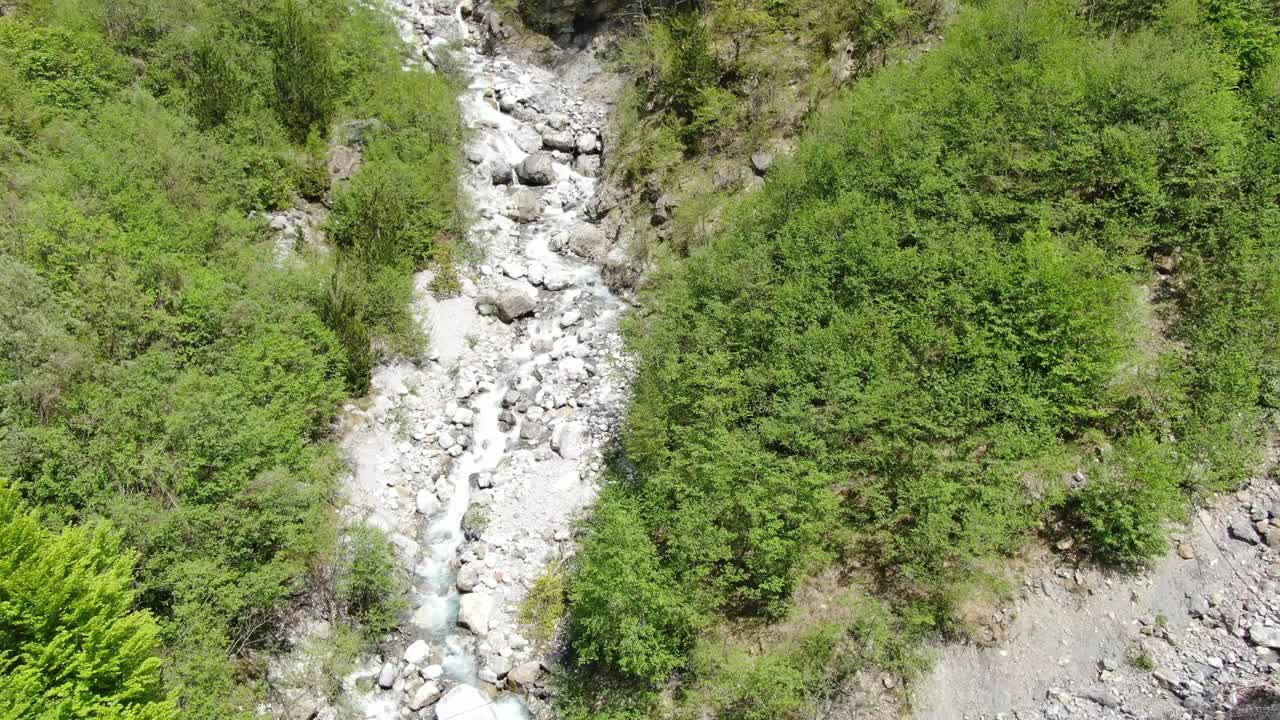 drone vista en albania en los alpes volando sobre un río de cristal con suelo rocoso con bosque verde en los lados en el