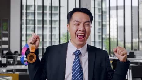 Close Up Of Asian Business Man In A Suit And Tie Looking At A Gold Medal Then Screaming Goal Celebrating Winning As The First Winner In Office