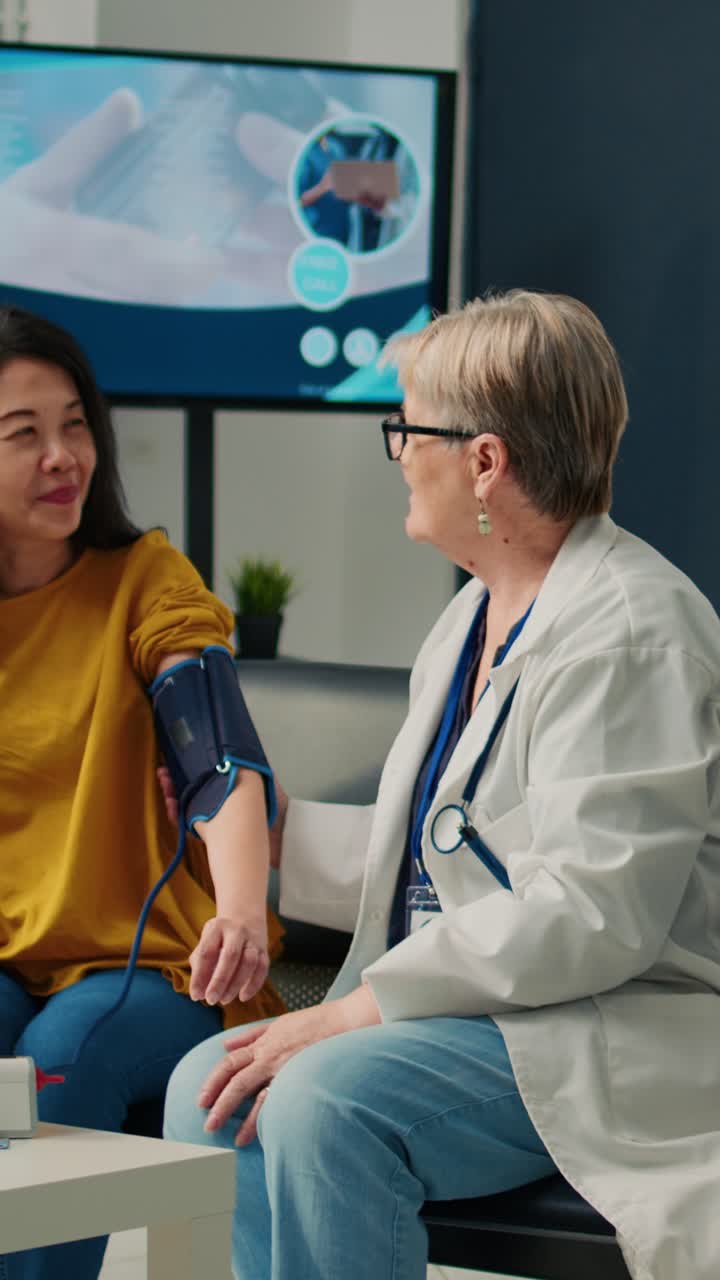 Vertical video: Elderly medic and asian woman doing hypertension measurement