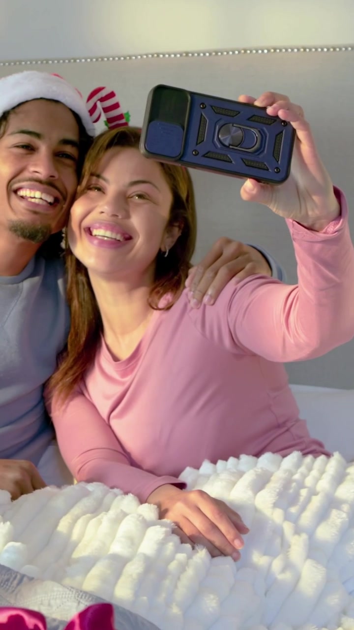 Video verticale: Donna in rosa che accetta una fascia offerta e si fa dei selfie sul letto con un uomo con il cappello di Babbo Natale.