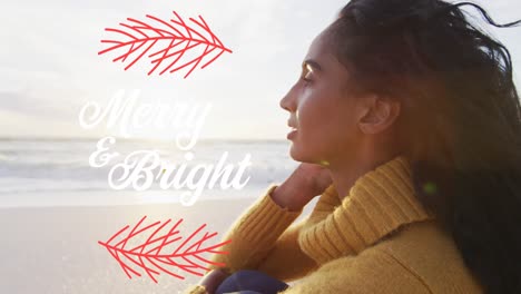 animation of merry and bright text over biracial woman at beach