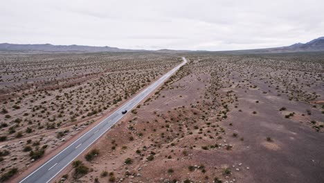 aerial drone shot of a car driving on a long isolated road in the desert
