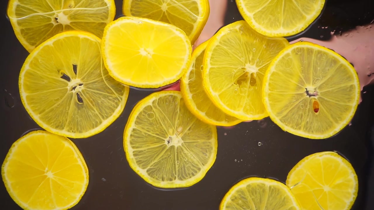 Fette di limoni cadono nell'acqua su una superficie trasparente. Vista dal basso. Movimento rallentato.