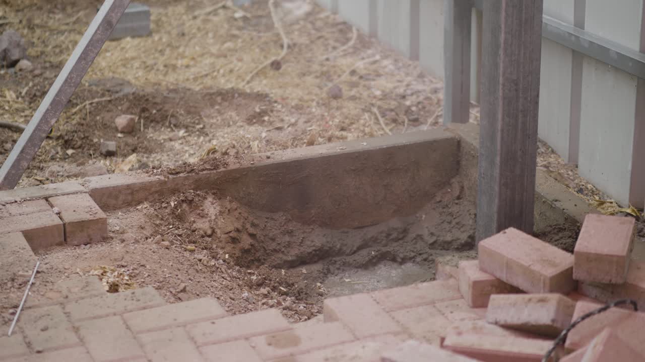 Person using shovel to fill the the base around a timber post that has been concreted into the gorund
