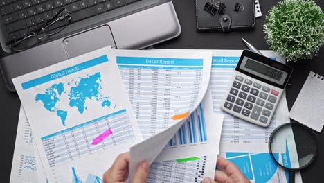 top view of businessman's hands working with financial reports. modern black office desk with laptop, notebook, pencil and a lot of things. flat lay table layout.