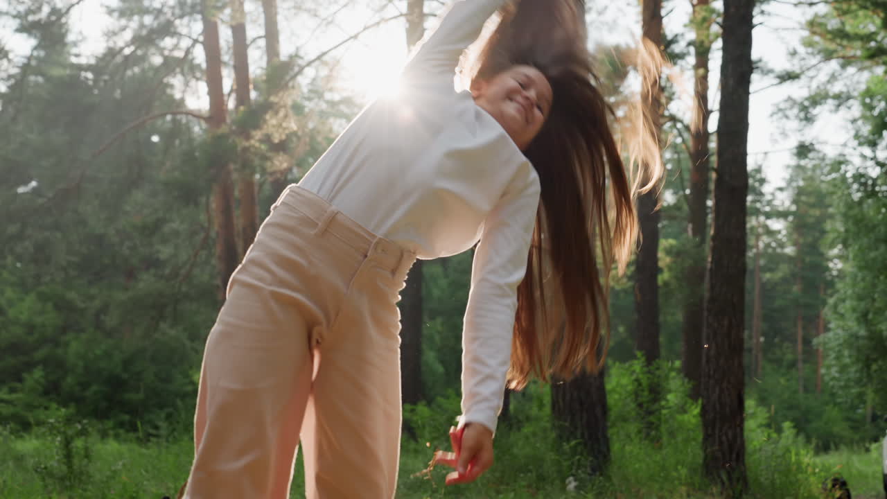 Older sister performing graceful acrobatic movement on picnic mat under shining sun beam in peaceful green forest, sunlight streaming through trees creating serene joyful summer outdoor moment