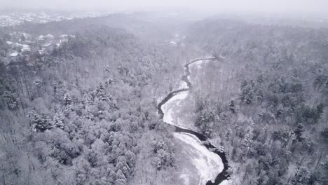 Gewundener-Fluss-Durchschneidet-Ein-Schneebedecktes-Tal-Während-Eines-Schneesturms-Mit-Frischem-Schnee,-Weißer,-Luftiger-Drohne,-Der-Im-Winter-Kanada-Schneit