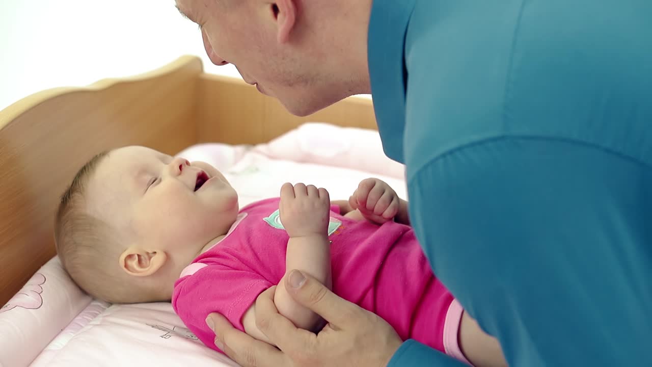 아빠는 변기 테이블에 누워 있는 작은 아기와 놀고, 아빠는 그녀를 향해  ⁇ 는다. 그녀는 눈을 감고 눈을  ⁇ 인다.