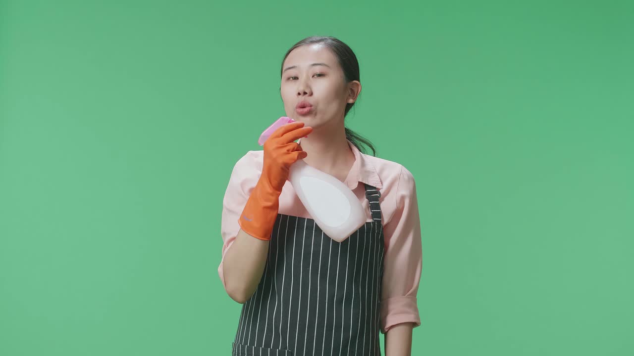 녹색 스크린 스튜디오에 서 있는 동안 총으로 불기 전에 아프론 스프레이를 가진 아시아 여성 집주인