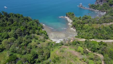 A-pristine-coastline-with-a-lush-forest,-white-sand,-and-crystal-blue-ocean-captured-from-an-aerial-perspective