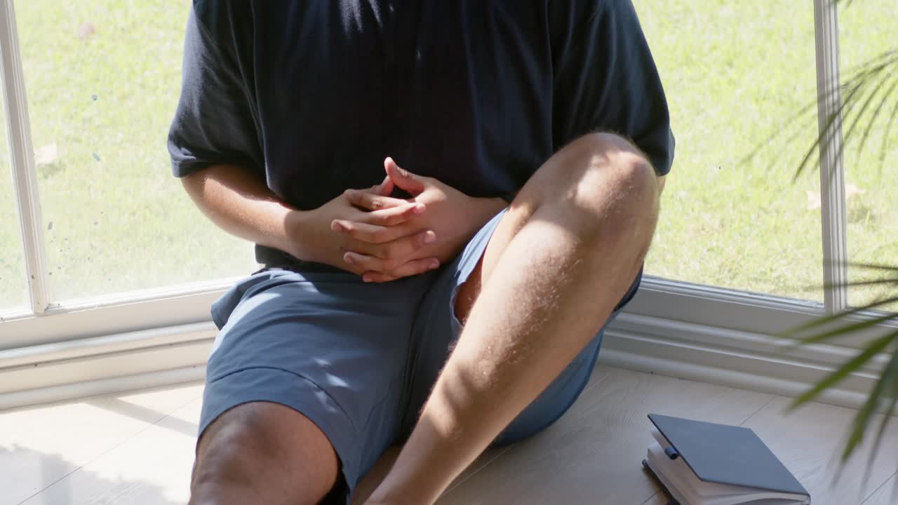 Camera pulling back, mid-adult African American man sitting by window, reflecting near notebooks