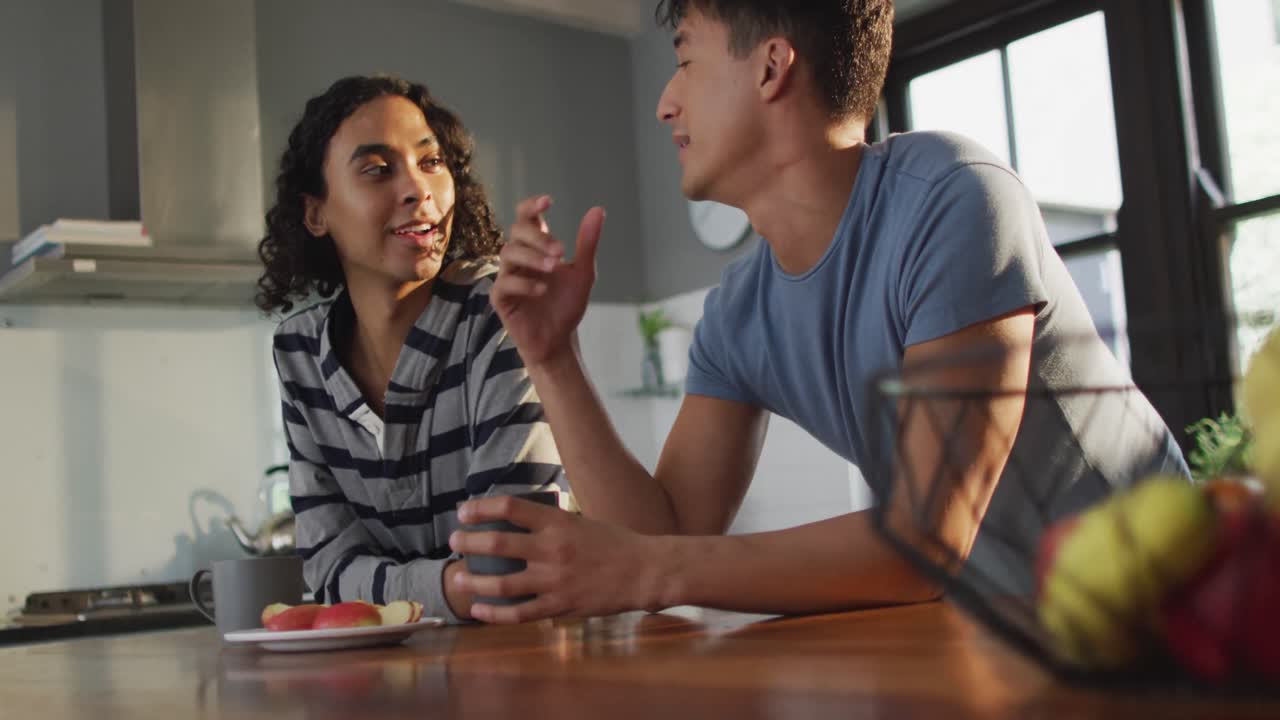 Casal masculino diverso feliz tomando café e conversando na cozinha