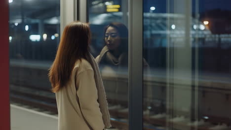 woman on a train station platform looking at her reflection at night