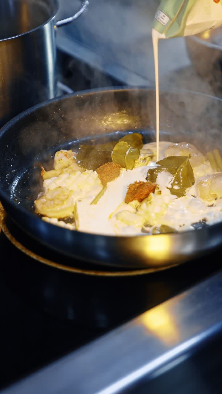 Cream is poured on the frying pan with food being fried. Cooking seafood at the restaurant. Close up. Vertical video.
