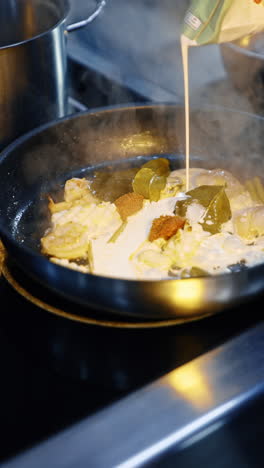 cream is poured on the frying pan with food being fried. cooking seafood at the restaurant. close up. vertical video.